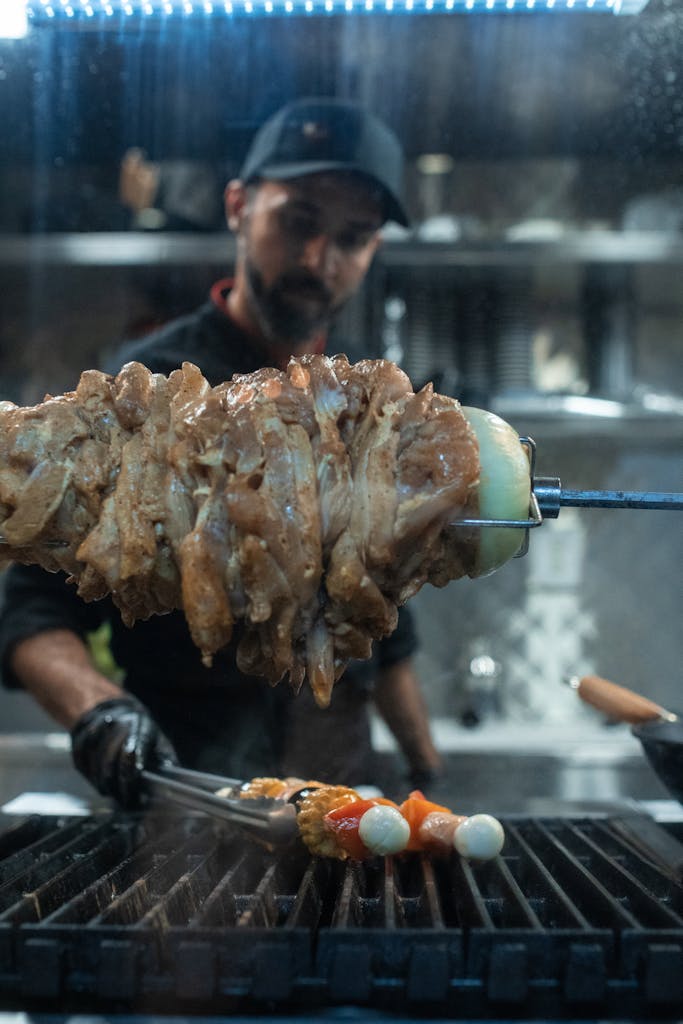 Chef prepares succulent meat skewers on grill in modern kitchen setting.