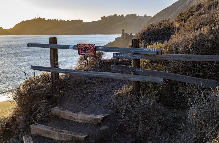 Rugged wooden fence along cliffside path with ocean view at sunset, ideal for travel and nature themes.