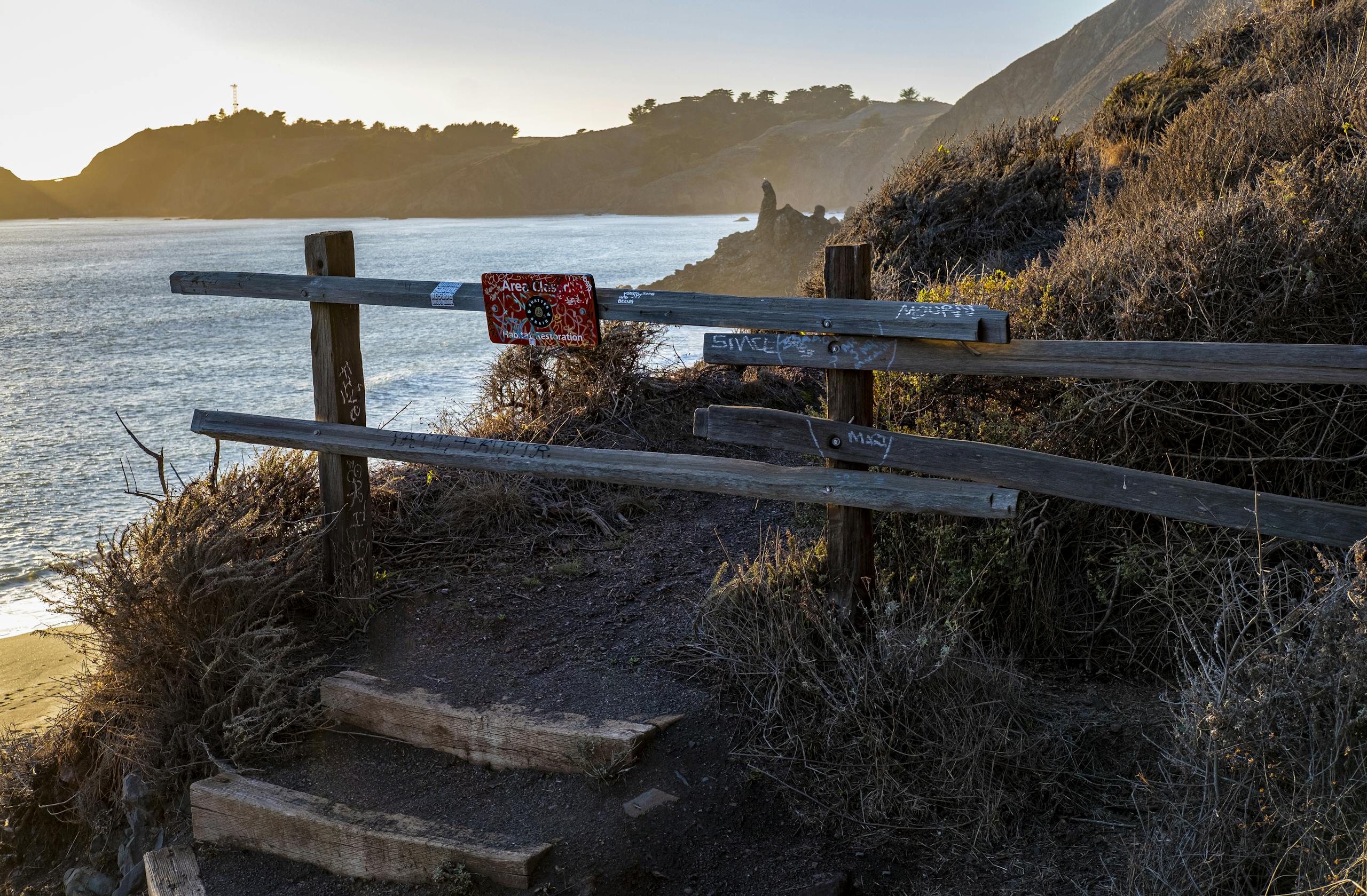 Rugged wooden fence along cliffside path with ocean view at sunset, ideal for travel and nature themes.